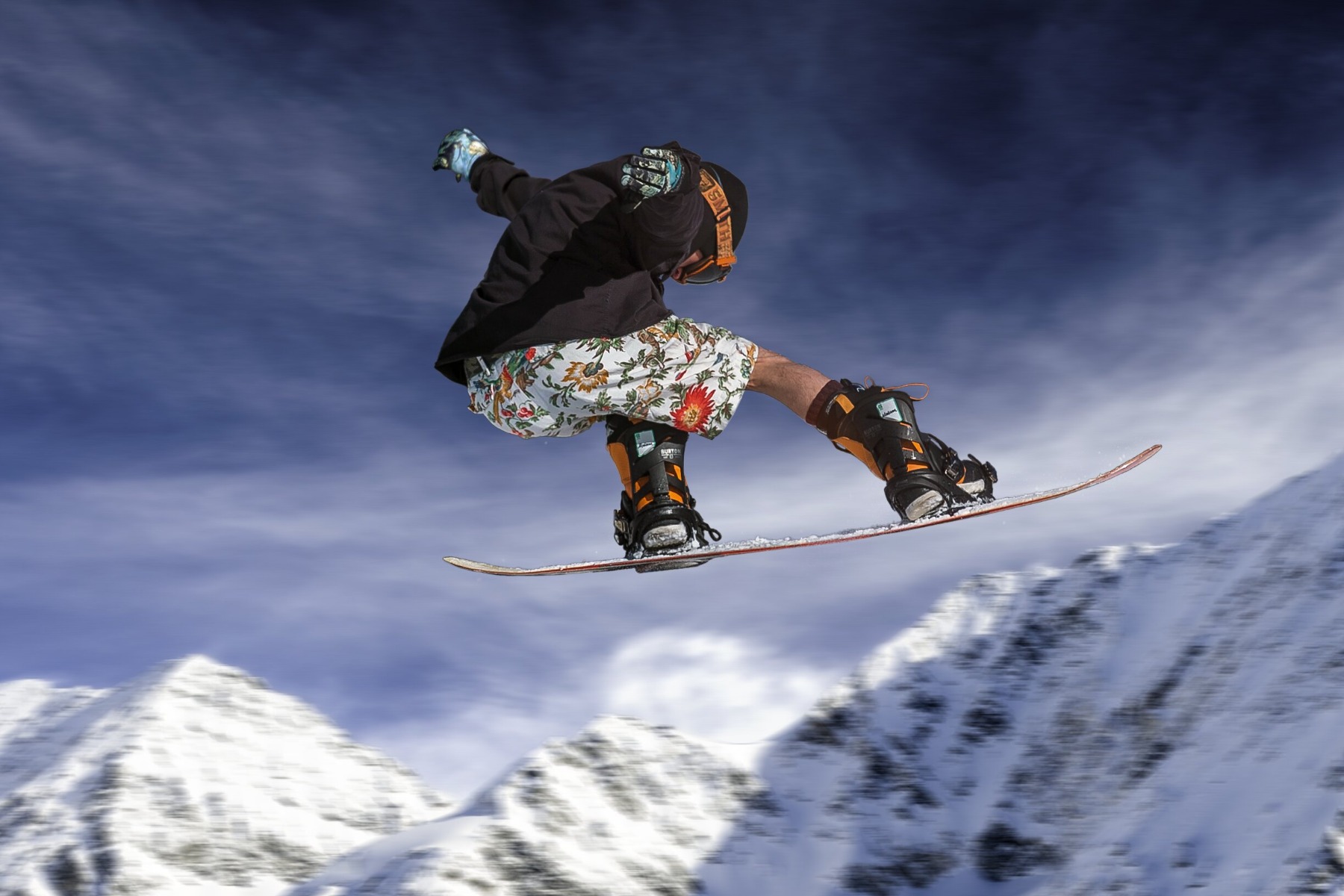 Man wearing floral shorts flying through air on snowboard